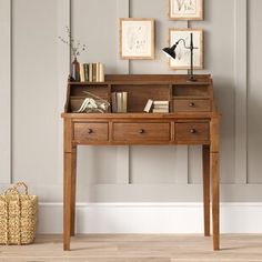 a wooden desk with drawers and two pictures on the wall above it, along with a wicker basket