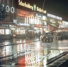 cars are driving down the street in the rain at night with buildings lit up behind them