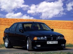 the black car is parked on the side of the road in front of an orange field