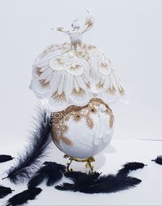 a white and gold bird with feathers around it's neck, sitting on top of an egg