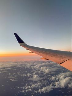 the wing of an airplane flying high above the clouds in the sky at sunset or dawn