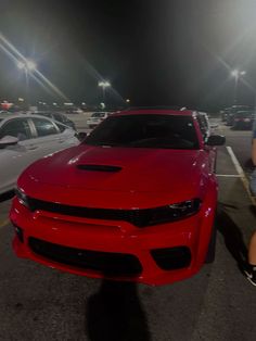 a red sports car parked in a parking lot next to another white car at night