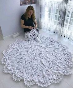 a woman is sitting on the floor making a crochet doily