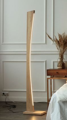 a wooden floor lamp on top of a bed next to a table with a plant