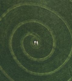 two people are standing in the middle of a circular grass field, looking down at each other