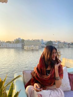 a woman sitting on top of a couch next to a lake talking on a cell phone