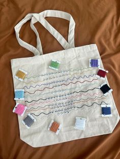 a tote bag with many different colored thread spools and pins on it