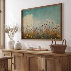 a painting is hanging on the wall next to a table with vases and baskets