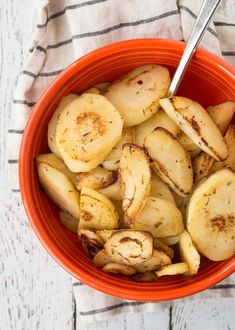 a red bowl filled with sliced potatoes on top of a striped cloth next to a fork