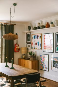 a dining room table with chairs and pictures on the wall above it, in front of a window