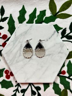 small silver and black earrings sitting on top of a white marble slab with holly leaves