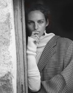 a black and white photo of a woman leaning against a window with her hand on her chin