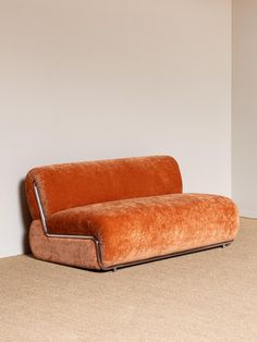 an orange couch sitting on top of a carpeted floor next to a white wall