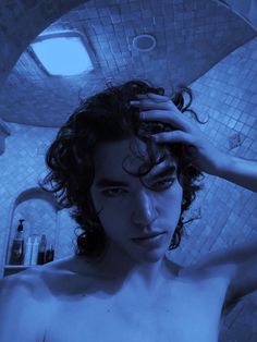 a man with curly hair standing in front of a bathtub holding his hand on his head