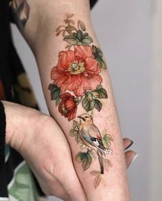 a woman with a bird and flower tattoo on her left arm is holding onto another person's hand