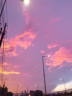 the sky is pink and purple with some clouds in it at night time, as well as street lights