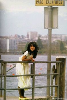 a woman in white dress standing on pier next to water and street sign that says paris eaux - vies