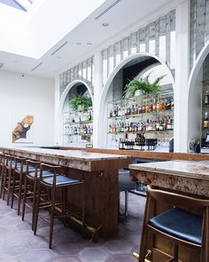 an empty bar with several stools and bottles on the wall behind it in a large room