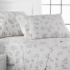 a bed with white sheets and black flowers on the comforter, next to a night stand