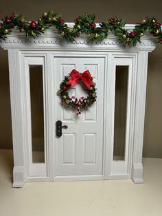 a christmas wreath on the front door of a white house with red bows and holly