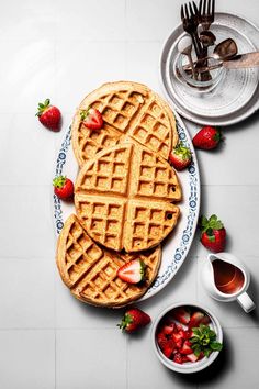 two waffles on a plate with strawberries next to each other and silverware