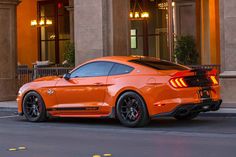 an orange mustang parked in front of a building