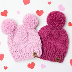 two knitted beanies with pom - poms on them sitting next to each other