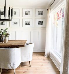 a dining room table with white chairs and pictures on the wall