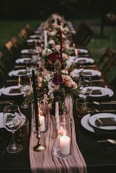 a long table is set with candles and plates for an elegant dinner party in the backyard