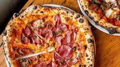 two pizzas sitting on top of white plates on a wooden table next to each other