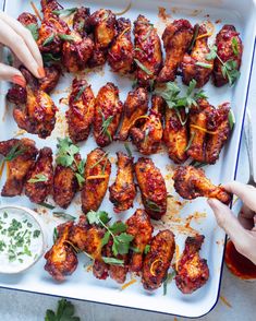 two hands reaching for chicken wings on a platter with dipping sauce and parsley