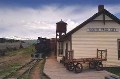 an old train sits at the station next to a small building with a water tower on top