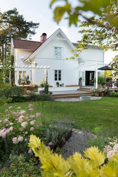 a large white house sitting in the middle of a lush green field with flowers around it