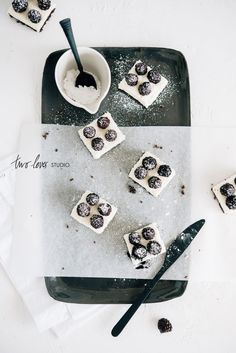 small desserts are arranged on a black and white platter with spoons next to them