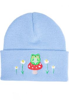 a blue beanie with a green frog sitting on top of a mushroom and daisies