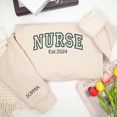 a sweater with the word nurse on it next to flowers