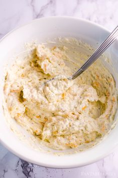 a white bowl filled with mashed potatoes on top of a marble counter next to a fork