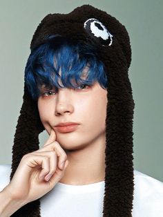 a young man with blue hair wearing a black cat hat and holding his hand to his chin