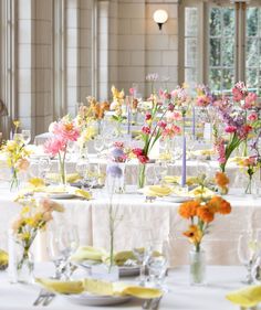 the tables are set with white linens and colorful flowers in vases on them