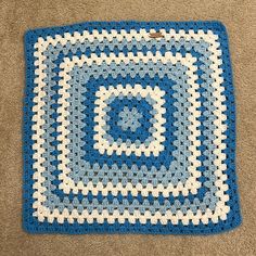 a blue and white crocheted square sitting on the floor next to a carpet