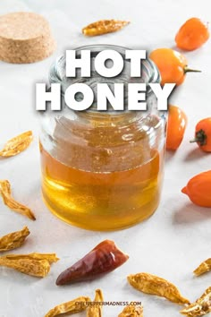 hot honey in a glass jar surrounded by dried oranges and chili peppers on a white surface