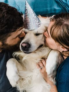 a man and woman laying next to a dog wearing a party hat