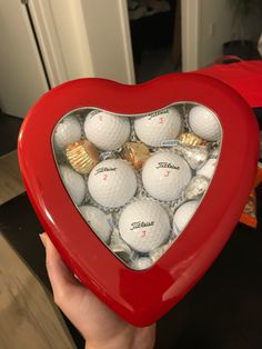 a heart shaped box filled with golf balls in the shape of a heart, held by someone's hand