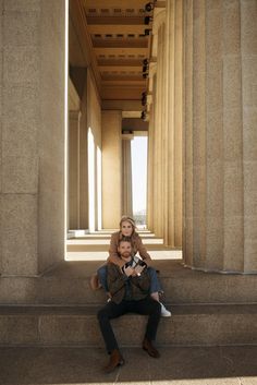 a man and woman sitting on the steps of a building with columns in the background