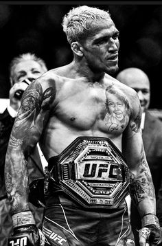 a black and white photo of a man with tattoos on his chest wearing a wrestling belt