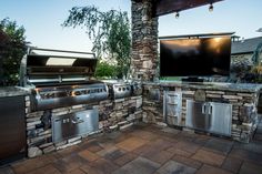 an outdoor kitchen with grills and television on the outside wall in front of it