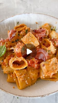 a white bowl filled with pasta covered in sauce and toppings on top of a marble table