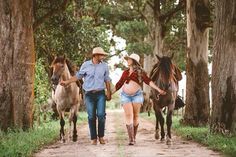 two people walking down a dirt road with horses and one person holding the hand of another horse