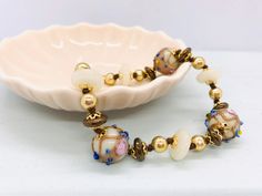 "Cute handmade vintage Venetian bracelet. The lampwork beads are decorated with aventurine swirls, blue dots and pink flowers. This style is called \"fiorato\" (in Italian fiore means flower) or \"wedding cake\" . ✔️ Length: 21 cm. This corresponds to a normal 19 cm. To compensate the diameter of the beads, the bracelet had to be a bit longer. ✔️ Shape glass beads: round 13 mm. The glass spacer beads are also Murano glass! ✔️ Color: cream ✔️ Decoration: flowers, dots, aventurine ✔️ Techniques: l Adjustable Murano Glass Beaded Bracelets With Round Beads, Adjustable Murano Glass Beaded Bracelets, Vintage Pearl Bracelet With Round Beads For Gift, Vintage Pearl Bracelet With Round Beads As Gift, Vintage White Round Beads Bracelets, Vintage White Bracelets With Round Beads, Vintage White Round Beaded Bracelets, Glass Hand-strung Bracelets For Gift, Vintage Spacer Beads Bracelets Gift