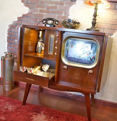 an old fashioned tv sitting on top of a wooden cabinet in front of a brick wall